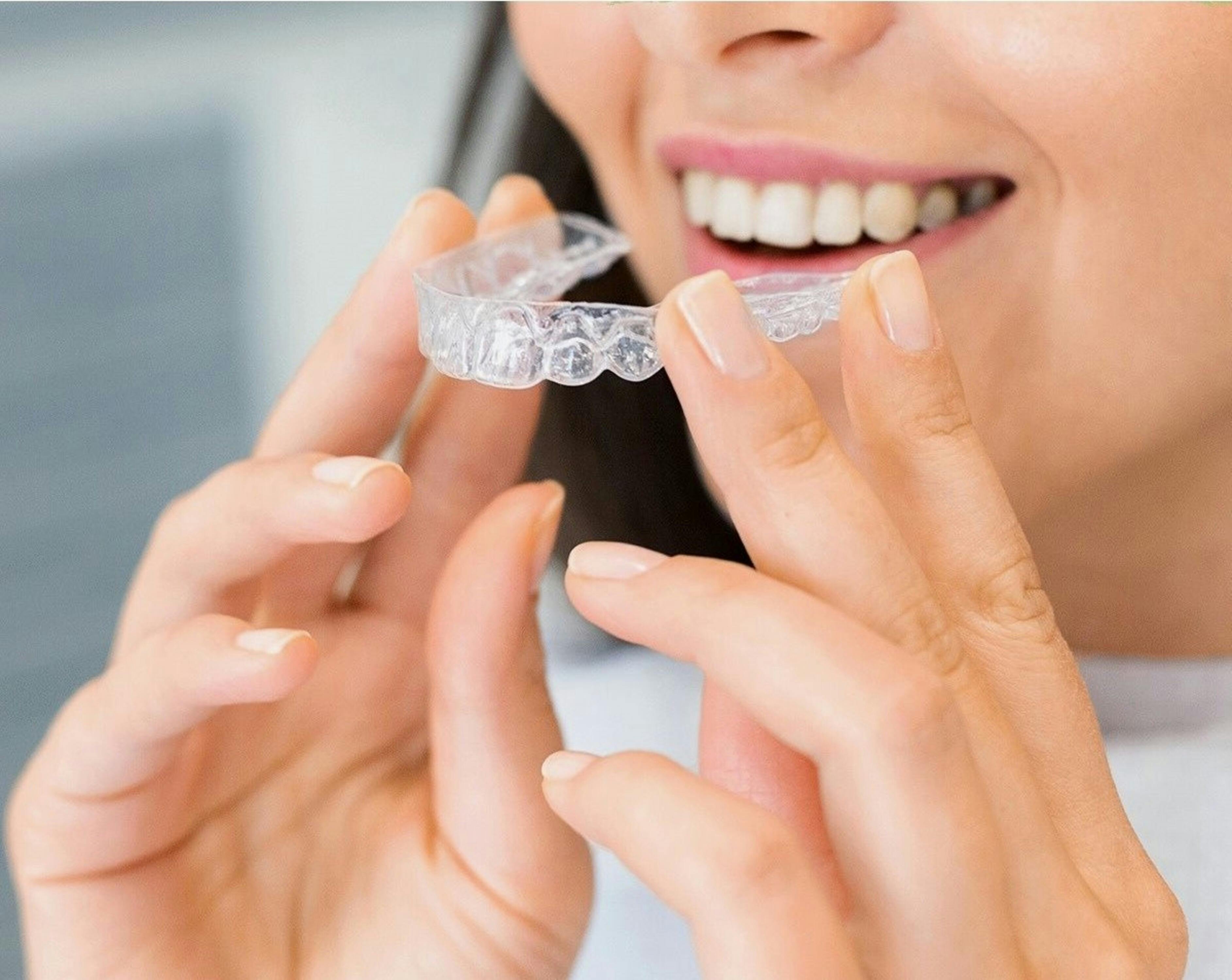 Woman holding clear dental aligners with beautiful smile